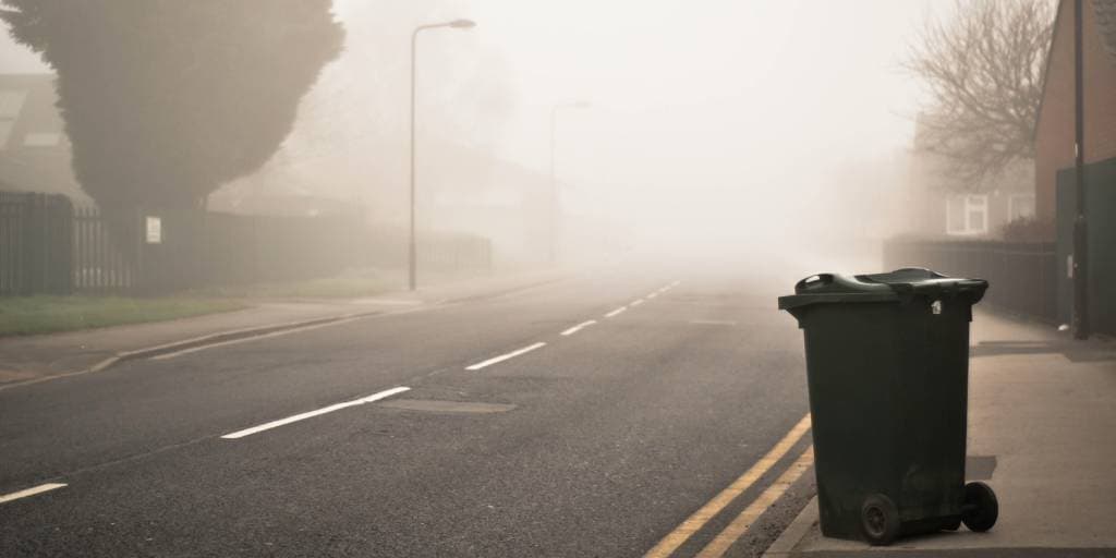 A garbage container next to the side of the road, ready to be collected.